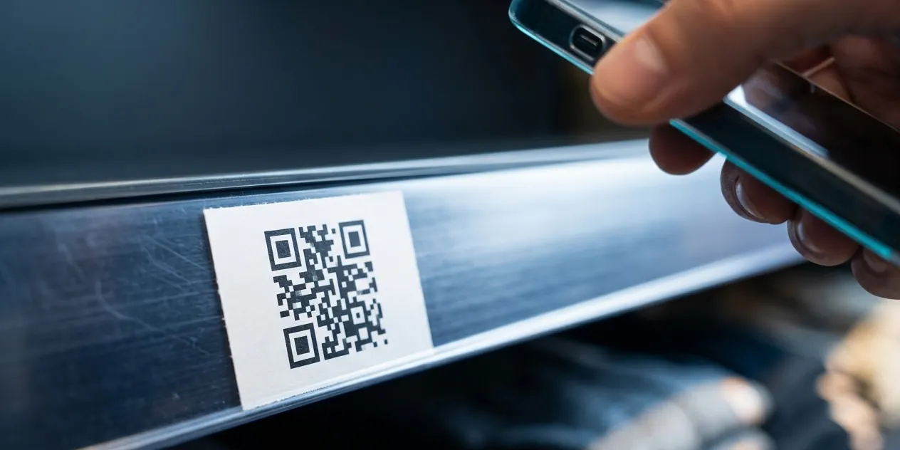 A printed QR label stuck on a shelf rail, with a phone aimed at it